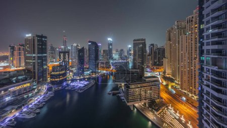 Foto de Vista aérea al puerto deportivo de Dubái rascacielos iluminados alrededor del canal con yates flotantes durante toda la noche con luces apagadas. Barcos blancos están estacionados en el club de yates - Imagen libre de derechos