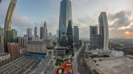 Foto de Panorama del distrito financiero internacional de Dubái transición día a día. Vista aérea de las torres de oficinas de negocios durante el amanecer. Rascacielos iluminados con hoteles y centros comerciales cerca del centro - Imagen libre de derechos