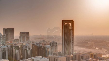 Foto de Salida del sol sobre rascacielos en el distrito de Barsha Heights y edificios de poca altura en la antena del distrito de Greens. Dubai skyline con cielo anaranjado en la mañana con el desierto en un fondo - Imagen libre de derechos