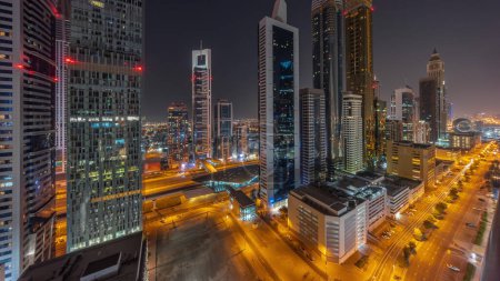 Téléchargez les photos : Vue aérienne du quartier financier international de Dubaï avec de nombreux gratte-ciel pendant la nuit avec des lumières éteintes. Trafic sur une route près d'un parking à plusieurs étages avec piscine sur le toit. Dubai, Émirats arabes unis. - en image libre de droit