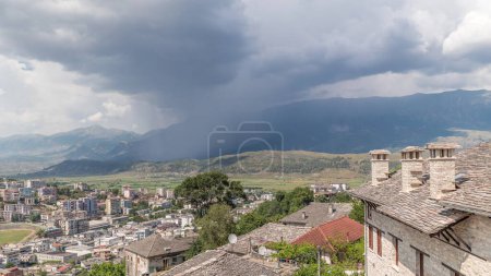 Foto de Panorama que muestra la ciudad de Gjirokastra desde el mirador con muchas casas históricas típicas con techos de piedra de Gjirokaster timelapse. Albania vista aérea al valle con nubes de lluvia y movimiento de ducha - Imagen libre de derechos