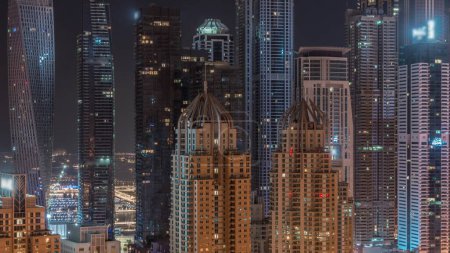 Téléchargez les photos : Les gratte-ciel de Dubai Marina avec des fenêtres clignotantes éclairées sur les bâtiments résidentiels les plus élevés pendant toute la nuit. Vue aérienne du quartier JLT - en image libre de droit