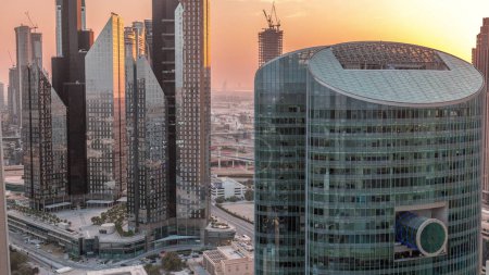 Téléchargez les photos : Coucher de soleil sur Dubaï gratte-ciel de centre financier international aérien. Ciel orange et soleil réfléchis par la surface en verre des tours - en image libre de droit