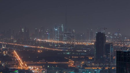 Photo for Dubai Downtown with financial district skyline row of skyscrapers with tallest tower aerial during night with lights. Overview in a far distance from Dubai marina rooftop. Villa houses and traffic - Royalty Free Image