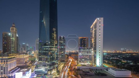 Téléchargez les photos : Dubai International Quartier financier transition jour-nuit. Vue aérienne panoramique des tours de bureaux d'affaires après le coucher du soleil. gratte-ciel avec hôtels et circulation sur une route près du centre-ville - en image libre de droit