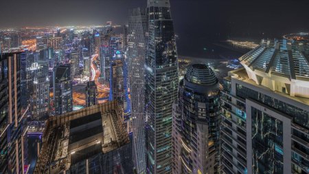 Téléchargez les photos : Panorama montrant Dubai Marina avec quartier JLT et JBR. Circulation sur l'autoroute entre les gratte-ciel la nuit aérienne. Tours modernes éclairées et chantier de construction - en image libre de droit
