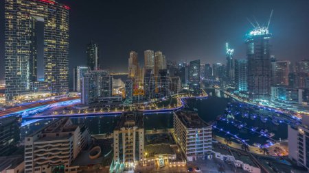 Téléchargez les photos : Dubai Marina panorama avec des bateaux garés dans le port et des gratte-ciel éclairés autour du canal aérien pendant toute la nuit. Tours du quartier JBR sur fond avec lumières éteintes - en image libre de droit