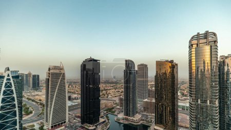 Téléchargez les photos : Grands bâtiments résidentiels à JLT district aérien pendant le coucher du soleil, qui fait partie du centre multi-commodités Dubaï quartier à usage mixte. Gratte-ciel avec de longues ombres et le soleil réfléchi par le verre - en image libre de droit