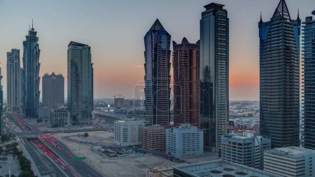 Foto de Skyline distrito de la bahía de negocios con la arquitectura moderna timelapse durante la puesta del sol desde arriba. Vista aérea de los rascacielos y torres de Dubái cerca de la autopista principal. Tráfico en una encrucijada - Imagen libre de derechos