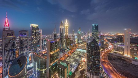 Foto de Vista panorámica del horizonte de los edificios de gran altura en Sheikh Zayed Road en Dubai día aéreo a la noche timelapse transición, Emiratos Árabes Unidos. Rascacielos iluminados en el Centro Financiero Internacional desde arriba - Imagen libre de derechos