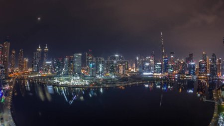 Foto de Panorama aéreo de Dubai Business Bay y Downtown durante toda la noche con los diversos rascacielos y torres a lo largo de la costa en el timelapse noche canal. Construcción con grúas cubiertas por niebla - Imagen libre de derechos