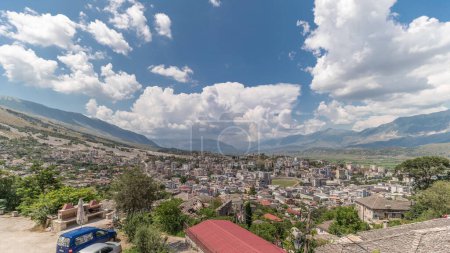 Foto de Panorama que muestra la ciudad de Gjirokastra desde el mirador con muchas casas históricas típicas con techos de piedra de Gjirokaster timelapse. Albania vista aérea al valle con nubes en un cielo azul - Imagen libre de derechos