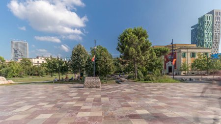 Foto de Panorama que muestra el monumento Skanderbeg y la mezquita Ethem Bey con teatro en la plaza principal en Tirana timelapse, Albania. Árboles verdes en un parque y rascacielos alrededor - Imagen libre de derechos