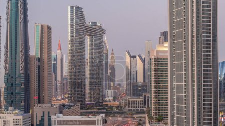 Photo for Futuristic towers and skyscrapers with traffic on streets in Dubai Downtown and financial district after sunset. Urban city skyline aerial day to night transition timelapse from above - Royalty Free Image