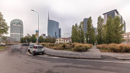 Photo for Panorama showing skyscrapers and towers from park with autumn trees and green lawn timelapse. Located between Piazza Gae Aulenti and the Isola district. Traffic on a road. Milan. Italy - Royalty Free Image