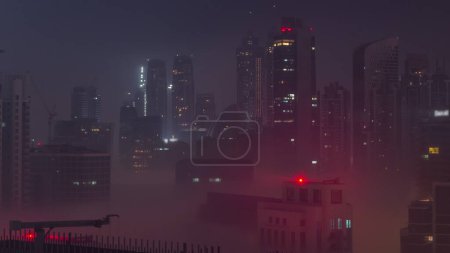 Photo for Dubai skyscrapers with illumination in business bay district during all night timelapse. Aerial view with fog from top of downtown in United Arab Emirates. Lights turning off - Royalty Free Image