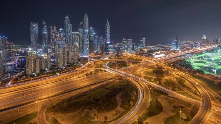 Photo for Panorama of Dubai Marina showing highway intersection spaghetti junction night timelapse. Illuminated tallest skyscrapers on a background. Aerial top view from JLT district. - Royalty Free Image