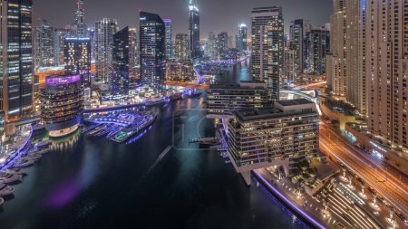 Téléchargez les photos : Vue aérienne des gratte-ciels de la marina de Dubaï et des tours jbr autour du canal avec des bateaux flottants de jour comme de nuit. Les bateaux blancs sont garés dans le yacht club après le coucher du soleil - en image libre de droit