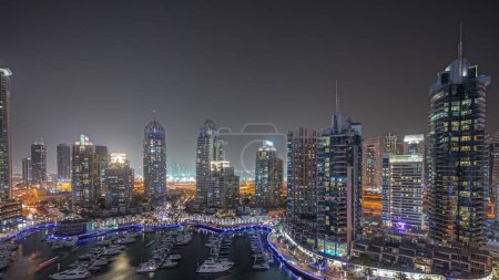 Photo for Panorama showing Dubai marina tallest skyscrapers and yachts in harbor aerial night timelapse. View at apartment buildings, hotels and office blocks, modern residential development of UAE - Royalty Free Image