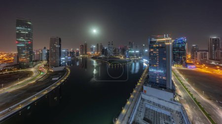Photo for Cityscape of skyscrapers in Dubai Business Bay with water canal aerial during night timelapse with Moon setting down. Modern skyline with illuminated towers and lights turning off - Royalty Free Image
