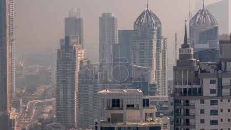 Téléchargez les photos : Dubai Marina et Media City quartiers avec brouillard matinal entre les gratte-ciel modernes et les immeubles de bureaux pendant le lever du soleil timelapse aérienne. Trafic sur le passage supérieur et l'intersection routière - en image libre de droit