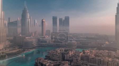 Foto de Vista aérea niebla de la mañana cubierto Dubai International Financial Centre timelapse distrito. Torres de oficinas y hoteles con rascacielos modernos y centro comercial durante el amanecer - Imagen libre de derechos