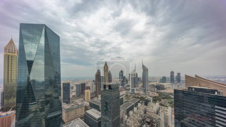 Photo for Panorama of futuristic skyscrapers in financial district business center in Dubai on Sheikh Zayed road timelapse. Aerial view from above with cloudy sky and shadows moving fast - Royalty Free Image