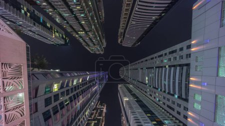 Téléchargez les photos : Regardez vers le ciel nocturne avec les plus hauts gratte-ciel avec des fenêtres éclairées. Perspective grand angle de la jungle urbaine dans la marina de Dubaï - en image libre de droit