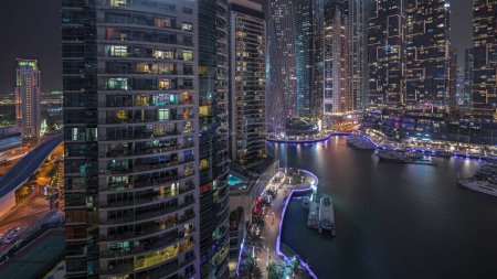Téléchargez les photos : Panorama montrant la baie de yacht de luxe dans la nuit aérienne de la ville timelapse dans la marina de Dubaï. Des gratte-ciel modernes le long de la promenade riveraine et des bateaux flottant dans le port - en image libre de droit