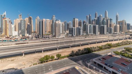 Foto de Panorama que muestra los rascacielos de Dubai Marina y la carretera Sheikh Zayed con timelapse aéreo de metro. Tráfico en una autopista cerca de torres modernas, Emiratos Árabes Unidos - Imagen libre de derechos