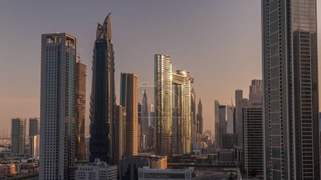 Téléchargez les photos : Tours futuristes et gratte-ciel avec circulation dans les rues de Dubaï Centre-ville et quartier financier. Urbain ville skyline aérienne matin timelapse pendant le lever du soleil. Lumière chaude et soleil réfléchis par le verre - en image libre de droit