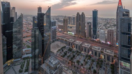Téléchargez les photos : Bâtiments de grande hauteur sur Sheikh Zayed Road à Dubaï transition aérienne du jour à la nuit timelapse panoramique, EAU. Gratte-ciels dans le quartier financier d'en haut. Maisons de promenade en ville et villas sur un fond - en image libre de droit