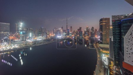 Foto de Panorama aéreo de Dubai Business Bay y Downtown con los diversos rascacielos y torres a lo largo de la costa en el canal noche a día timelapse transición. Lugar de construcción con grúas antes del amanecer - Imagen libre de derechos