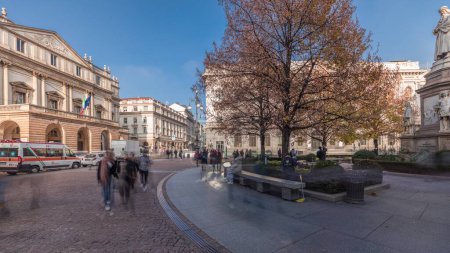 Foto de Panorama que muestra el teatro La Scala timelapse y un pequeño parque frente al edificio histórico con un monumento a Leonardo da Vinci y sus estudiantes. Gente caminando y sentada en un banco - Imagen libre de derechos