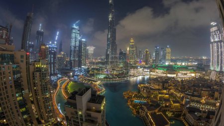 Téléchargez les photos : Gratte-ciel s'élevant au-dessus du centre-ville de Dubaï de jour à la nuit transition timelapse, centre commercial et fontaine entourés de bâtiments modernes vue panoramique aérienne avec ciel nuageux coucher de soleil - en image libre de droit