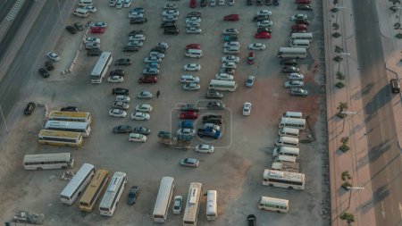 Téléchargez les photos : Vue aérienne d'un parking avec de nombreuses voitures et bus en rangées timelapse pendant toute la journée avec des ombres se déplaçant rapidement. Espace libre sur un sable - en image libre de droit
