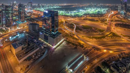 Foto de Enorme cruce de carreteras entre el distrito JLT y la ciudad de los medios de comunicación intersecado por la noche aérea Sheikh Zayed Road después de la puesta del sol. Campo de golf cerca de torres y rascacielos con mucho tráfico - Imagen libre de derechos