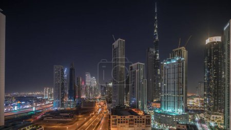 Téléchargez les photos : Panorama montrant la vue aérienne de Dubaï Downtown et Business Bay skyline avec de nombreuses tours éclairées timelapse de nuit. Zone de luxe dans la ville urbaine intelligente. gratte-ciels et immeubles de grande hauteur d'en haut - en image libre de droit