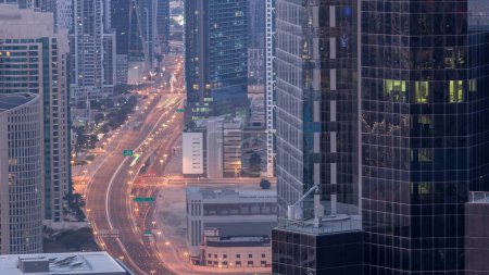 Téléchargez les photos : Vue aérienne d'en haut à des intersections animées à Dubaï, nuit à jour, période de transition. Voitures conduisant directement dans les deux sens de la route avant le lever du soleil. Quartier des affaires gratte-ciel - en image libre de droit