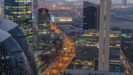 Foto de Vista del horizonte de los edificios de gran altura en la carretera curva en Dubai noche aérea al día timelapse transición, Emiratos Árabes Unidos. Rascacielos de oficinas en el Centro Financiero Internacional desde arriba antes del amanecer - Imagen libre de derechos