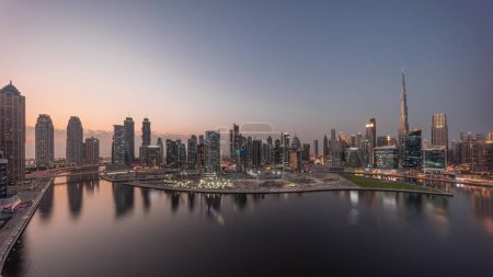 Foto de Panorama aéreo de Dubai Business Bay y Downtown con los diversos rascacielos y torres a lo largo de la costa en el canal de día a noche timelapse transición. Lugar de construcción con grúas después del atardecer - Imagen libre de derechos