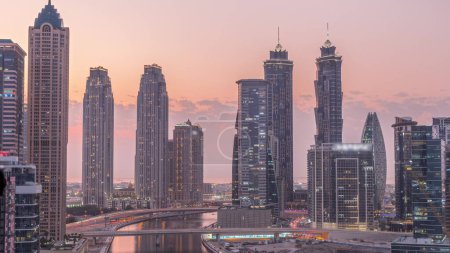 Téléchargez les photos : Paysage urbain avec des gratte-ciel de Dubai Business Bay et canal d'eau aérien de jour comme de nuit passage timelapse. Skyline moderne avec des tours résidentielles et de bureaux sur le front de mer après le coucher du soleil - en image libre de droit
