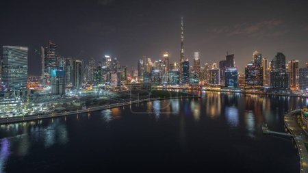 Photo for Panorama showing aerial view to Dubai Business Bay and Downtown with the various skyscrapers and towers along waterfront on canal night timelapse. Construction site with cranes - Royalty Free Image