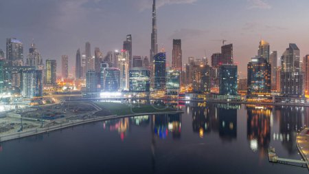 Téléchargez les photos : Vue aérienne vers Dubai Business Bay et le centre-ville avec les différents gratte-ciels et tours le long du front de mer sur le canal nuit à jour passage timelapse. Site de construction avec grues avant le lever du soleil - en image libre de droit