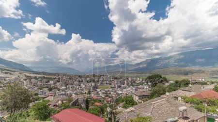 Téléchargez les photos : Panorama montrant la ville de Gjirokastra du point de vue avec de nombreuses maisons historiques typiques avec des toits en pierre de Gjirokaster timelapse. Albanie vue aérienne de la vallée avec des nuages sur un ciel bleu - en image libre de droit
