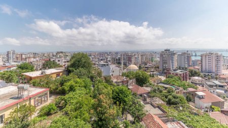 Téléchargez les photos : Panorama montrant la vue aérienne du centre-ville (vieille ville) et le port de Durres timelapse du point de vue, Albanie. Beaucoup de maisons avec des toits rouges et des arbres verts d'en haut avec des nuages sur elle ciel - en image libre de droit