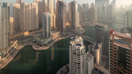 Téléchargez les photos : Vue de différents gratte-ciel dans le plus haut quartier résidentiel de Dubai Marina et JBR quartier aérien nuit à jour timelapse de transition avec canal artificiel. Nombreuses tours et yachts au lever du soleil - en image libre de droit