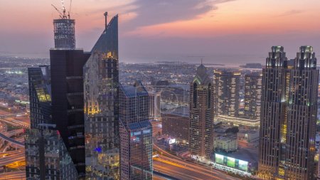 Foto de Edificios de gran altura en Sheikh Zayed Road en Dubai día aéreo a noche timelapse transición, Emiratos Árabes Unidos. Rascacielos en el distrito financiero internacional desde arriba. Casas de paseo por la ciudad y villas en un fondo - Imagen libre de derechos