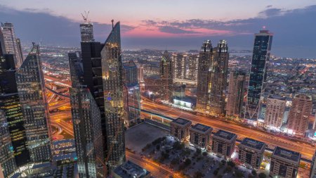 Téléchargez les photos : Bâtiments de grande hauteur sur Sheikh Zayed Road à Dubaï passage aérien du jour à la nuit timelapse, EAU. gratte-ciel dans le quartier financier international d'en haut. Maisons de promenade de la ville et circulation sur le fond - en image libre de droit