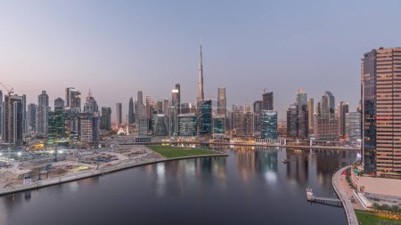 Photo for Aerial panoramic view to Dubai Business Bay and Downtown with the various skyscrapers and towers along waterfront on canal day to night transition timelapse. Construction site with cranes after sunset - Royalty Free Image